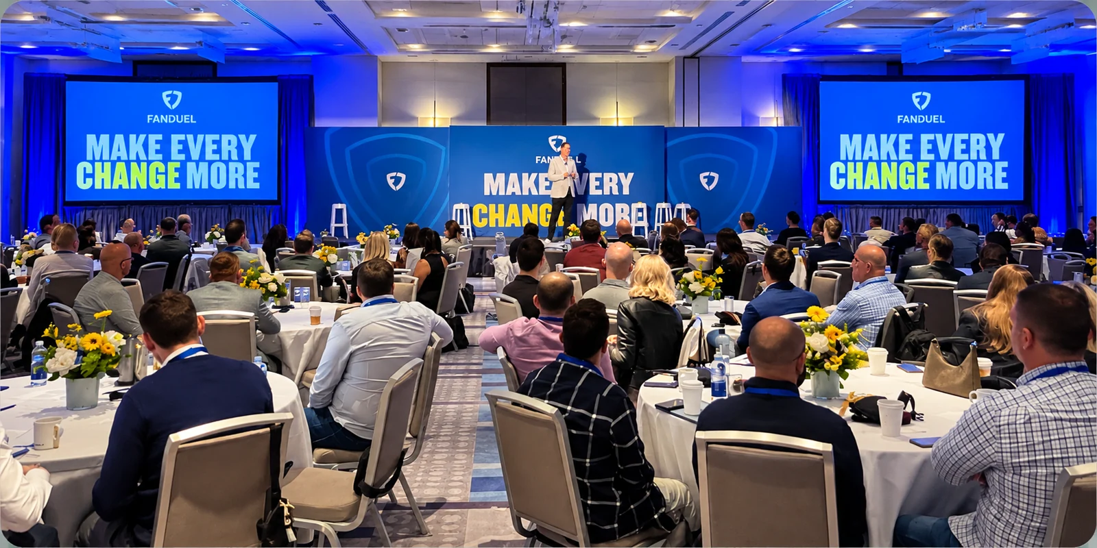 FanDuel corporate business offsite presentation in a ballroom, with attendees seated at round tables facing a branded stage